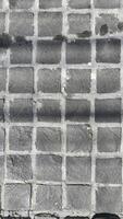 image features textured gray cobblestone pavement with grid pattern, showcasing unique surface details and shadows photo