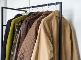 A row of autumn and spring coats in earthy tones hanging on a sleek clothing rack. photo