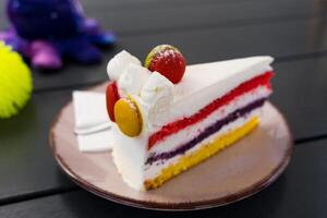 Close-up of a colorful layered cake with macarons on top, served on a plate in a cozy cafe. photo