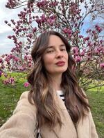 Caucasian woman with air touch hair coloring taking a selfie near blooming magnolia tree in spring. photo