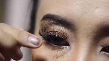 de cerca de un mujer cara mientras aplicando falso pestañas para un glamoroso mirar. mejorando belleza con cosmético procedimientos. video