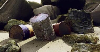 Rusty barrels and rocks scattered on a sandy shore by the ocean at sunset video