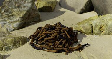 Rusty chain tangled among stones on a sandy beach during daytime video
