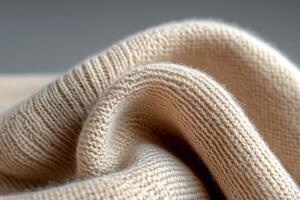 A close-up view reveals a tightly woven beige knitted fabric with soft folds. The interplay of light and deep shadows creates a rich, moody texture, emphasizing the fabric's quality photo