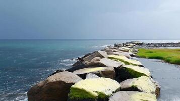 Coastal view of a rocky jetty extending into the ocean under a moody sky with greenery photo