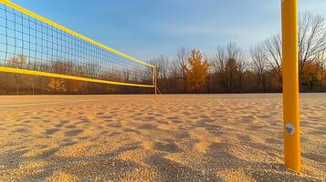 Sunset over an empty beach volleyball court with a net and autumn trees in the background photo