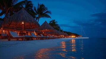 Tranquil beach scene at twilight with thatched huts, illuminated lounge chairs, and calm waters photo