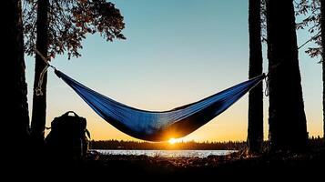 Tranquil sunset view with a hammock between trees and a backpack by a serene lakeside photo