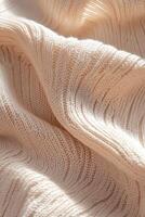 Beige knitted fabric displays a structured geometric texture enhanced by sharp directional lighting. The interplay of light and shadow highlights the depth and intricacy of the material photo
