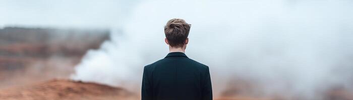 A man in a formal outfit stands alone in an empty, vast landscape. His smooth, featureless face is enveloped by swirling mist, evoking a sense of deep contemplation photo