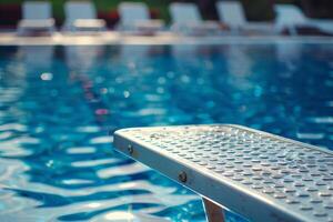 A pool with a ladder and chairs in the background photo