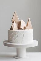 This stylish cake showcases a minimalist approach with sharp, angular fondant textures and striking metallic geometric shapes on top, ideal for contemporary celebrations or events photo