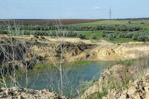 a huge blue lake in a quarry. deciduous forests and fields around. the horizon is visible. an artificial lake among fields. dry grass in the foreground photo
