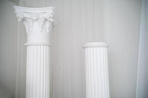 element of antique column in interior. photo zone for photo sessions. two white columns are located in interior. white chiffon fabric is planted
