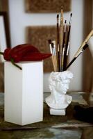 three red large peppers and a glass for brushes in the form of an antique head. hot red pepper on a white cube and a classic head made of plaster photo