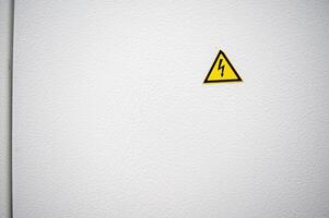 Warning sign about high voltage on electrical equipment. There is space for text. The sign is yellow, triangular in shape on a white metal surface. A sign above a door. High quality photo