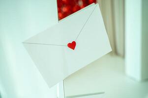 Kraft white envelope sealed with a small cute heart. close-up view from the front. against the background of a light room with red color in the interior. photo