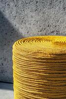 Bright yellow woven rope stacked in round shape against textured gray wall, creating vibrant contrast. sunlight enhances color and texture, adding depth to scene photo
