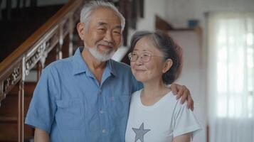 portrait of an asian elderly couple standing in a room with a staircase in the background. The asian man is on the left side of the image photo