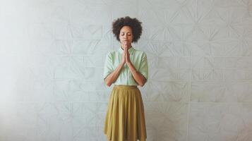 woman standing in front of a white wall with a geometric pattern. She is wearing a light green button-down shirt and a mustard-colored skirt. photo
