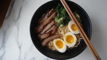 top view of a bowl of ramen noodles with two hard-boiled eggs on top. The bowl is black and is placed on a white marble countertop photo