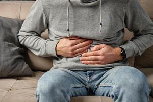 Man clutching stomach in pain while sitting on couch. Person suffering from digestion problems photo