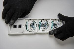 Close-up of an electrician wearing gloves installing power socket on white wall photo