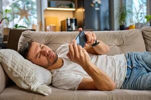 Man relaxing on couch using smartphone at home photo