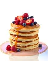 Stack of pancakes with fresh berries and maple syrup isolated on white background photo