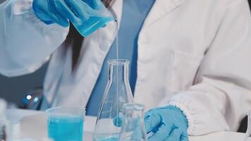 A person in a lab coat is pouring blue liquid into a beaker video