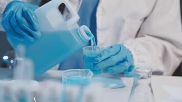 A person in a lab coat pouring blue liquid into a container video