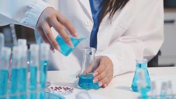 A woman in a lab coat is pouring blue liquid into a flask video