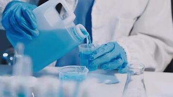 A person in a lab coat pouring blue liquid into a container video