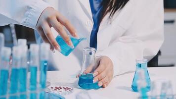 A woman in a lab coat is pouring blue liquid into a flask video