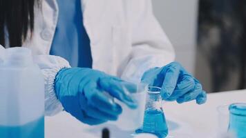 A person in a lab coat and gloves is holding a blue liquid video