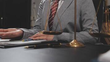 A man in a suit is sitting at a desk with a scale of justice video