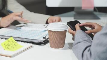 Two people are sitting at a desk with a cup of coffee and a cell phone video