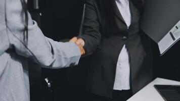 Two business people shaking hands in front of a computer video