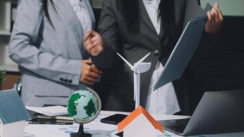 Two business people standing around a table with a laptop and a wind turbine video