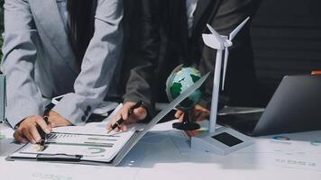 Business people working on a laptop and a paper with a wind turbine video