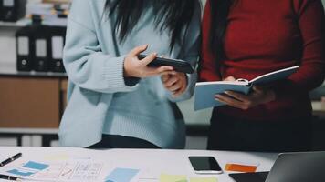 Two women standing at a desk with a laptop and a notebook video