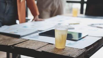 A glass of juice sits on a table next to a laptop video