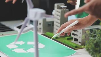 A man is drawing a recycling symbol on a paper with a wind turbine in the background video