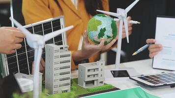 A group of people are working on a project with a model of a building and wind turbines video