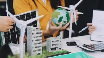 A group of people are working on a project with a model of a solar panel and wind turbines video