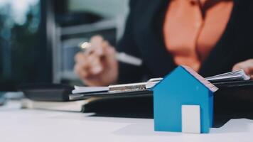 A woman is working on her laptop and a house model is sitting on the table video