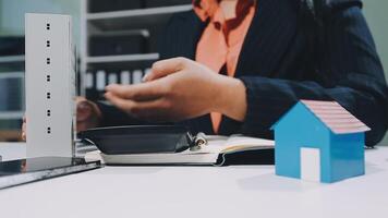 A woman is holding a house model in front of a laptop video