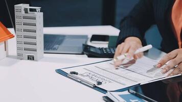 A person is working on paperwork at a desk with a house and a pen video