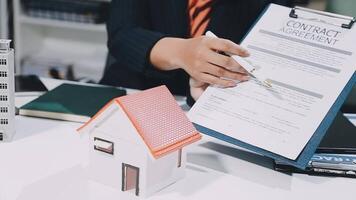 A real estate agent is holding a contract agreement with a house model video