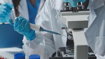 Two people in lab coats and gloves are working on a microscope video